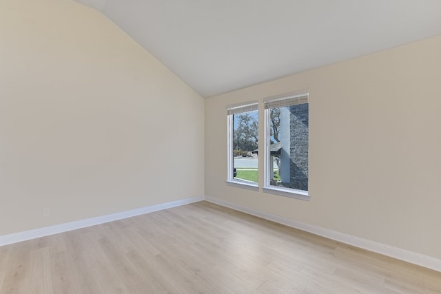 spare room with baseboards, light wood-style floors, and vaulted ceiling