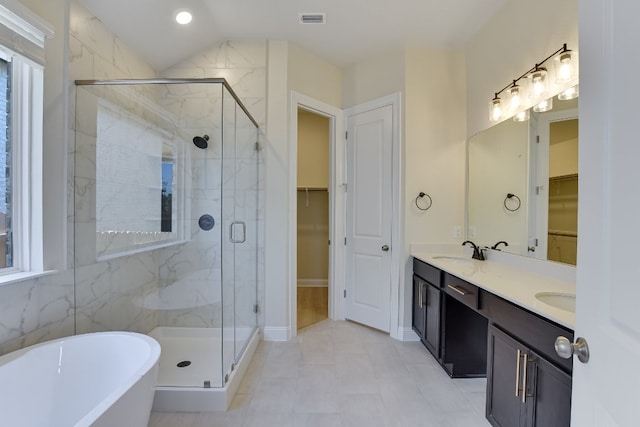 bathroom with visible vents, a walk in closet, a stall shower, a freestanding tub, and a sink