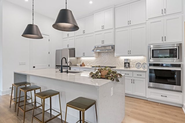 kitchen with decorative light fixtures, white cabinetry, stainless steel appliances, and an island with sink