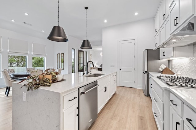 kitchen with pendant lighting, white cabinets, stainless steel appliances, and an island with sink