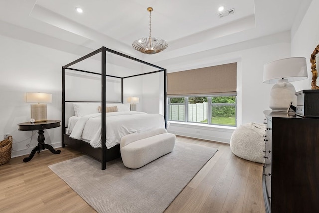 bedroom with a tray ceiling and light hardwood / wood-style flooring