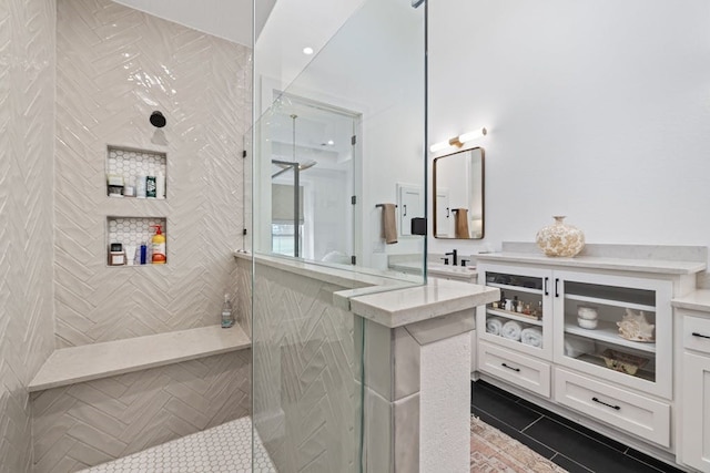 bathroom with tile patterned flooring, tiled shower, and vanity