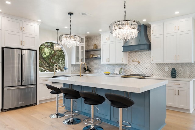 kitchen with custom exhaust hood, hanging light fixtures, white cabinetry, and high end fridge