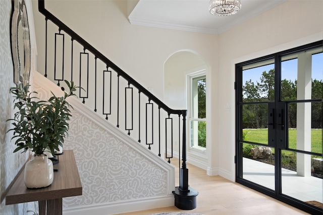 foyer entrance featuring french doors, ornamental molding, light hardwood / wood-style flooring, and a notable chandelier