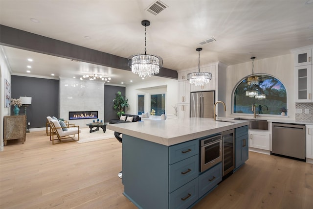 kitchen featuring white cabinetry, a center island with sink, appliances with stainless steel finishes, a tiled fireplace, and tasteful backsplash