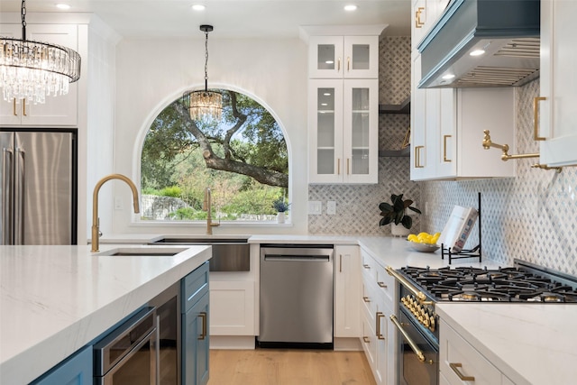 kitchen with white cabinetry, appliances with stainless steel finishes, exhaust hood, and an inviting chandelier