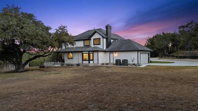 back house at dusk with a garage, cooling unit, and a yard