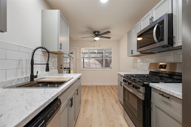 kitchen with tasteful backsplash, ceiling fan, sink, light hardwood / wood-style flooring, and appliances with stainless steel finishes