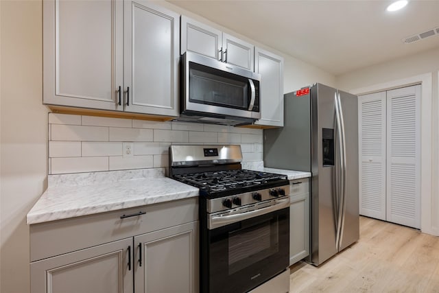 kitchen with gray cabinets, stainless steel appliances, backsplash, light hardwood / wood-style flooring, and light stone counters