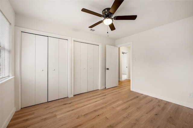 unfurnished bedroom with ceiling fan, light hardwood / wood-style floors, and two closets