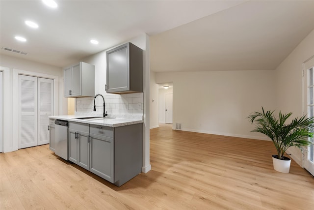 kitchen featuring tasteful backsplash, stainless steel dishwasher, sink, light wood-type flooring, and gray cabinetry