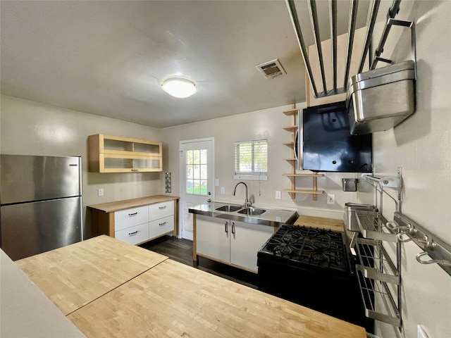 kitchen featuring dark wood-type flooring, stainless steel refrigerator, black range with gas stovetop, white cabinets, and sink