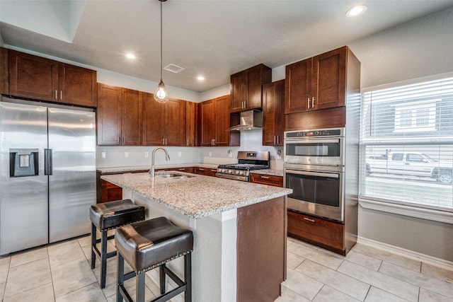 kitchen featuring wall chimney exhaust hood, decorative light fixtures, stainless steel appliances, sink, and a center island with sink