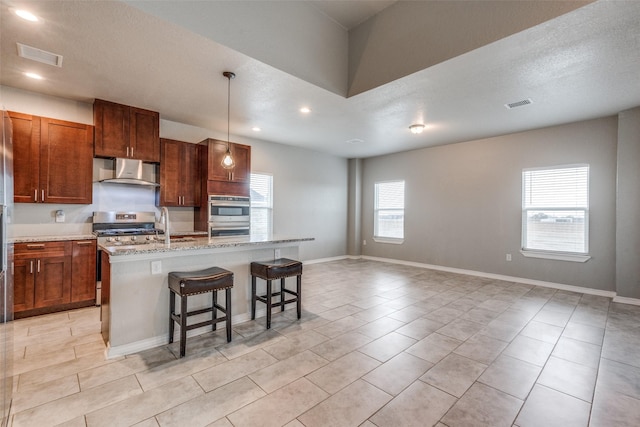 kitchen featuring a wealth of natural light, wall chimney exhaust hood, an island with sink, and a breakfast bar area