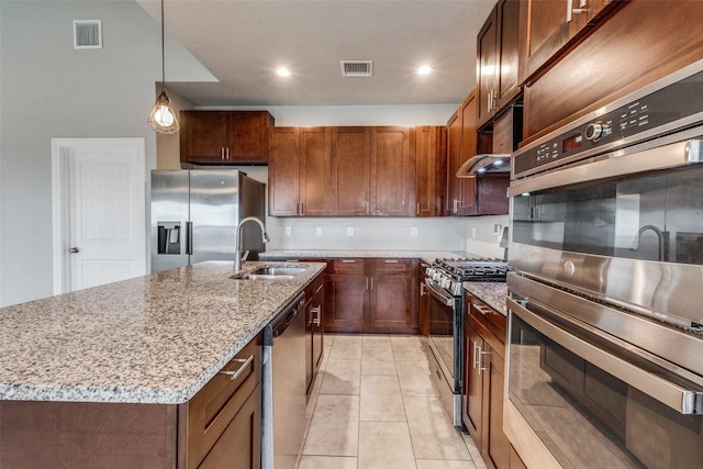 kitchen featuring decorative light fixtures, sink, appliances with stainless steel finishes, an island with sink, and light stone counters