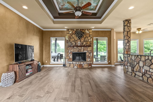 living room featuring ceiling fan, a wealth of natural light, ornamental molding, and a stone fireplace