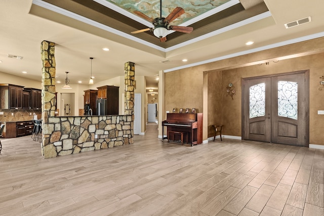 interior space with light wood-type flooring, ceiling fan, crown molding, and a raised ceiling