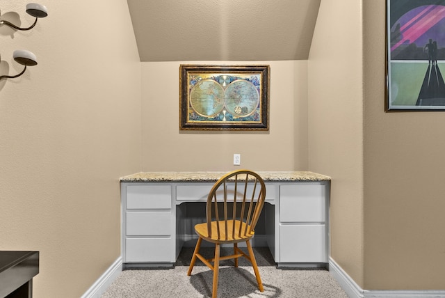 carpeted office space with lofted ceiling and built in desk