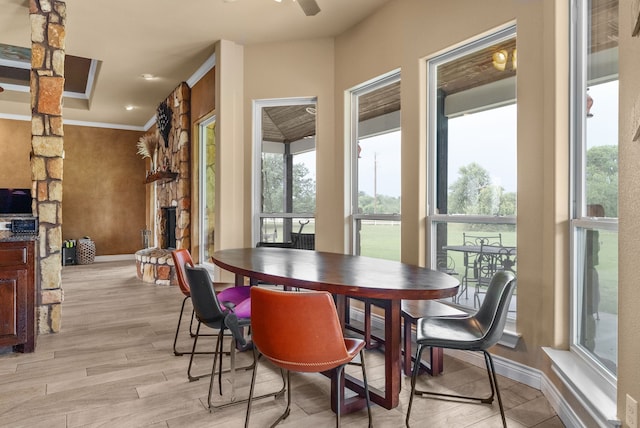 dining space with ceiling fan, a stone fireplace, ornamental molding, and light hardwood / wood-style flooring