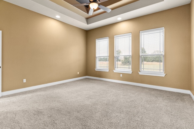 empty room with ceiling fan, carpet flooring, and a raised ceiling