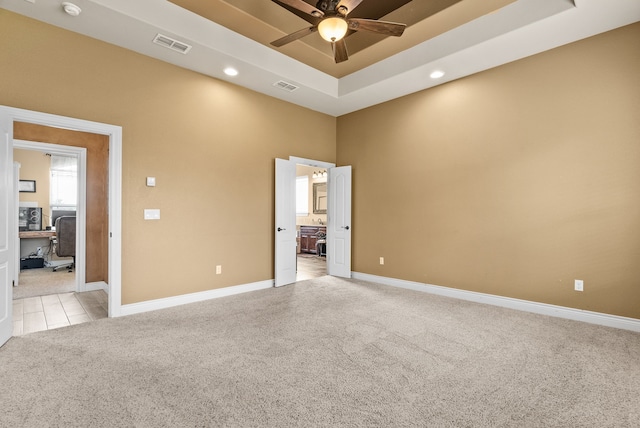 spare room featuring ceiling fan, a tray ceiling, and light carpet