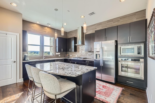 kitchen featuring wall chimney range hood, a center island, pendant lighting, a breakfast bar, and stainless steel appliances