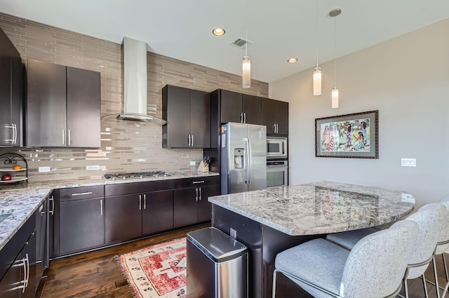 kitchen featuring a kitchen bar, appliances with stainless steel finishes, wall chimney range hood, and a kitchen island