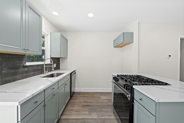 kitchen featuring black gas range, backsplash, stainless steel dishwasher, light stone counters, and sink