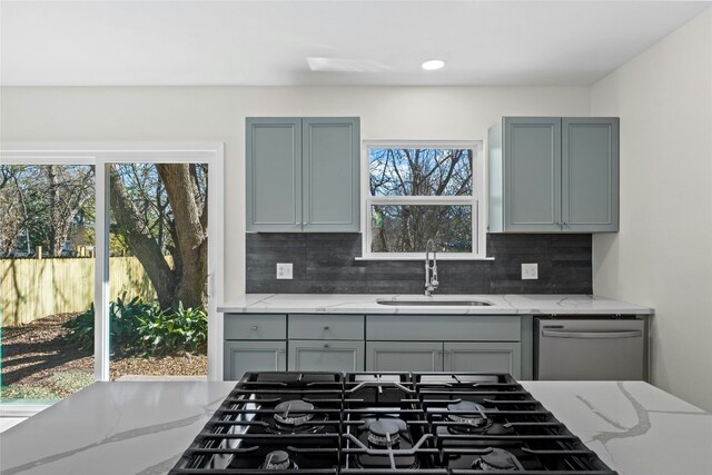 kitchen featuring stainless steel dishwasher, a wealth of natural light, sink, and light stone counters