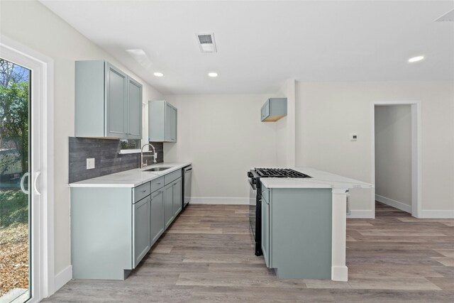 kitchen with dishwasher, gas stove, decorative backsplash, sink, and light hardwood / wood-style flooring