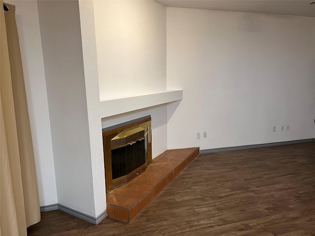 unfurnished living room with dark wood-type flooring and a tiled fireplace