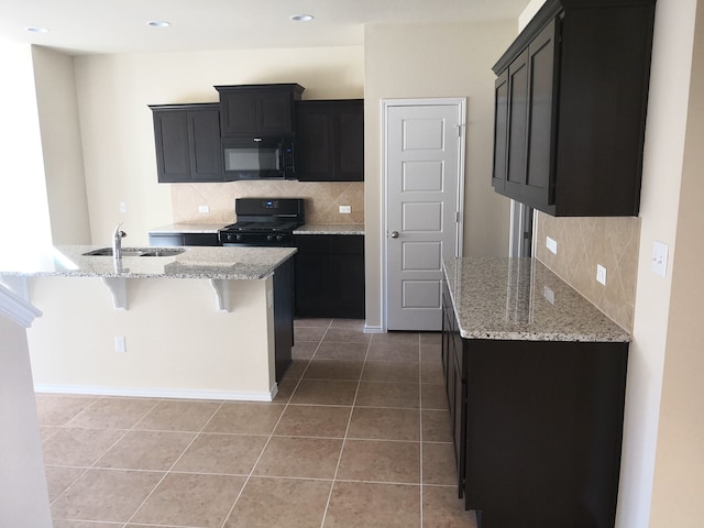 kitchen featuring tasteful backsplash, tile patterned floors, light stone countertops, black appliances, and sink