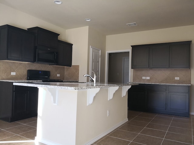 kitchen featuring light stone countertops, range with electric cooktop, a center island with sink, and dark tile patterned floors