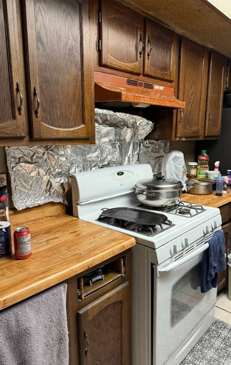 kitchen with wood counters, light tile patterned flooring, dark brown cabinets, and white gas range oven