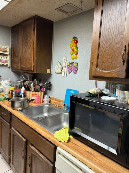 kitchen with butcher block countertops, dark brown cabinets, sink, and light tile patterned floors