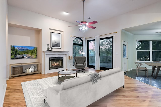 living room with ceiling fan, a tiled fireplace, and light hardwood / wood-style floors