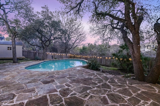 pool at dusk featuring a shed and a patio