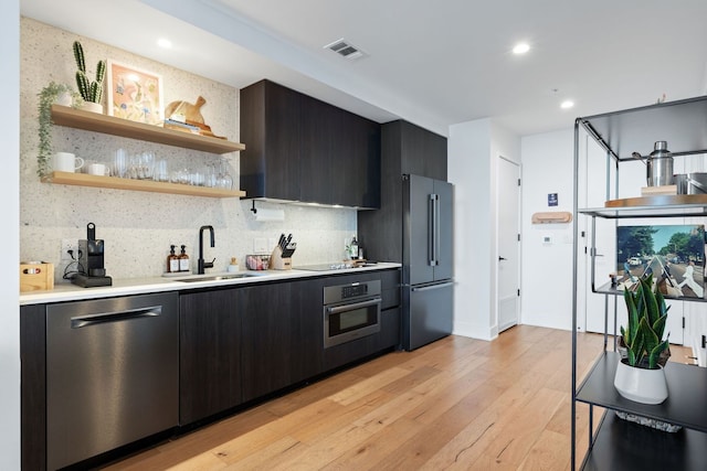 kitchen featuring appliances with stainless steel finishes, light hardwood / wood-style flooring, tasteful backsplash, and sink