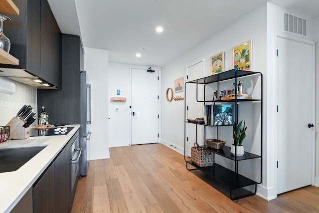 kitchen with backsplash, sink, stainless steel refrigerator, light hardwood / wood-style flooring, and black electric cooktop