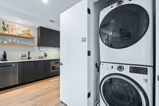 washroom with stacked washer / drying machine, light hardwood / wood-style floors, and sink