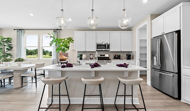 kitchen featuring stainless steel appliances, an island with sink, hanging light fixtures, and white cabinetry