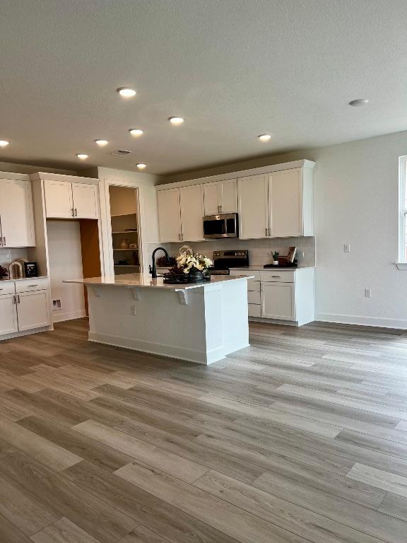 17101 Astral Ln, Manor, TX 78653 - kitchen with appliances with stainless steel finishes, white cabinetry, light wood finished floors, recessed lighting, and a center island with sink