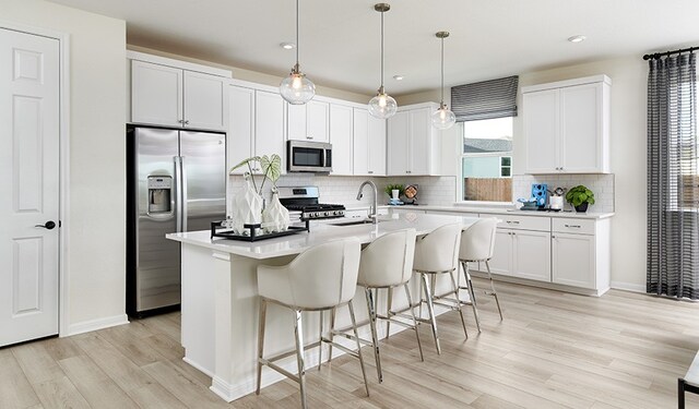 kitchen with sink, appliances with stainless steel finishes, pendant lighting, a kitchen island with sink, and white cabinets