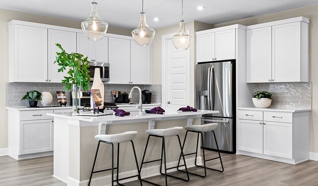 kitchen featuring stainless steel appliances, a kitchen island with sink, white cabinets, and decorative light fixtures