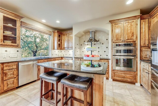 kitchen featuring tasteful backsplash, dark stone countertops, a center island, light tile patterned floors, and stainless steel appliances