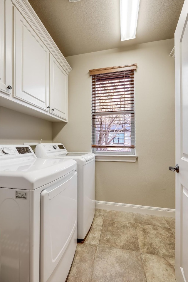 clothes washing area featuring cabinets, a textured ceiling, and washing machine and clothes dryer