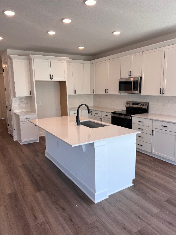 10016 Ephemeral Dr, Manor, TX 78653 - kitchen featuring stainless steel microwave, range with electric stovetop, white cabinetry, dark wood-style floors, and an island with sink