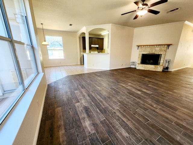 unfurnished living room featuring ceiling fan, ornamental molding, and a stone fireplace