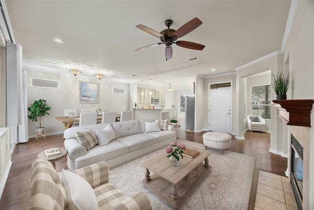 living room with wood-type flooring, ceiling fan, crown molding, and a tiled fireplace