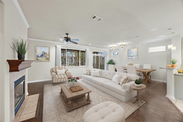 living room with ceiling fan, light wood-type flooring, a tiled fireplace, and ornamental molding